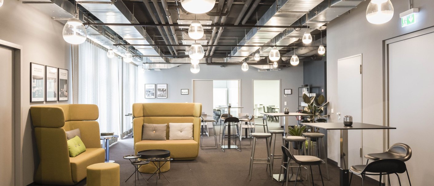 Moderne Lobby mit gelben Sofas, hohen Tischen und Hockern. Deckenbeleuchtung und Pflanzen schaffen eine einladende Atmosphäre., © Design Offices GmbH