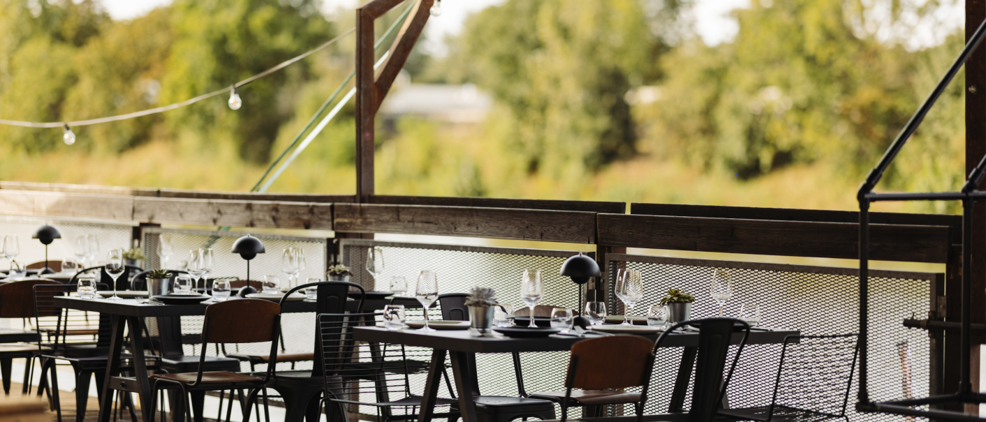 A stylish outdoor area with tables and chairs on a wooden terrace, surrounded by green nature., © Fridas Pier A stylish outdoor area with tables and chairs on a wooden terrace, surrounded by green nature., © Fridas Pier