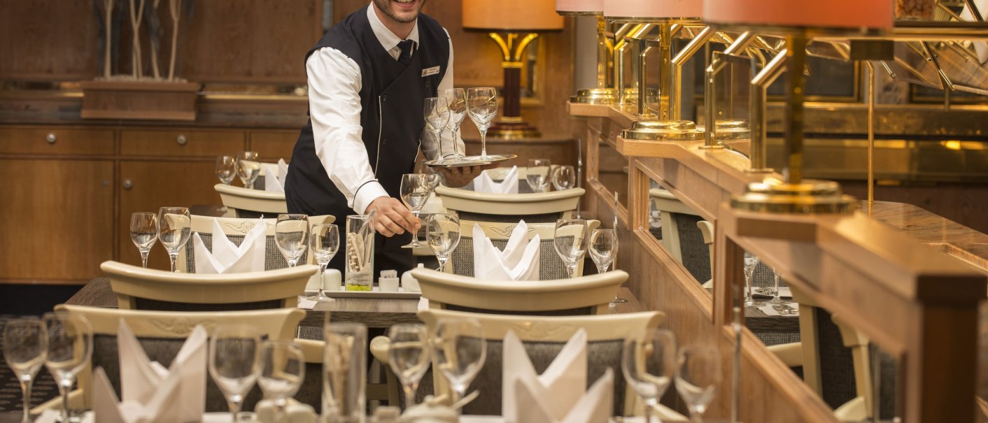 A waiter in the restaurant of the Maritim Hotel Stuttgart sets tables with glasses and napkins. Elegant furnishings with warm light., © Jesco Birkhahn