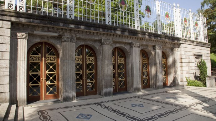 A terrace with a marble floor, ornate wooden doors, and a decorative fence. The sun casts shadows on the floor., &copy; csusannmeissner