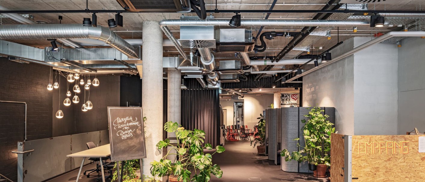 Reception area with industrial design, visible ventilation pipes, plants and a desk. A sign welcomes visitors., &copy; Design Offices
