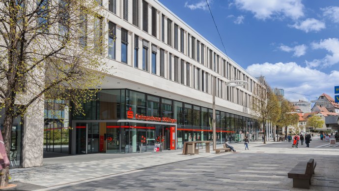 The SparkassenForum B&ouml;blingen with its modern glass fa&ccedil;ade and pedestrian zone. People strolling in sunny weather. Trees with fresh leaves., &copy; ccbs