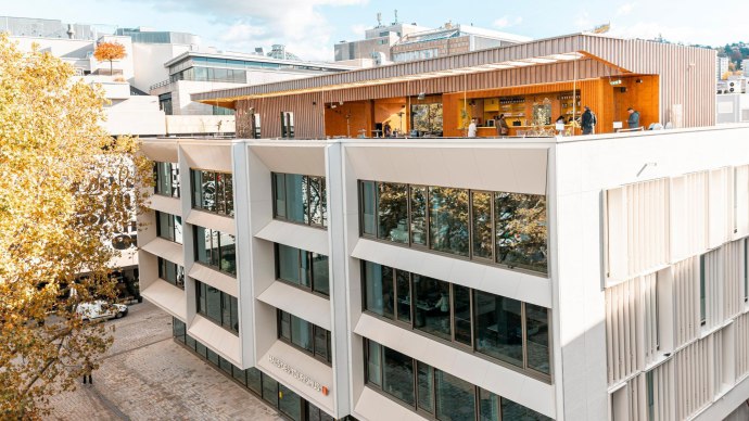 Modern fa&ccedil;ade of the House of Tourism with large glass windows and a terrace. People stroll along the paved square in front of it., &copy; SMG Stuttgart Marketing GmbH - Sarah Schmid