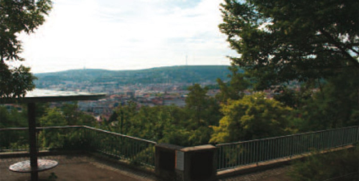 Aussichtsplattform mit Geländer, umgeben von Bäumen, bietet Blick auf eine Stadt und Hügel im Hintergrund., © Stuttgart-Marketing GmbH