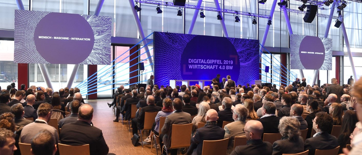 Teilnehmer sitzen in einem modernen Konferenzraum beim Digitalgipfel 2019 Wirtschaft 4.0 BW. Auf Bildschirmen steht "Mensch - Maschine - Interaktion"., © Carl Benz Arena