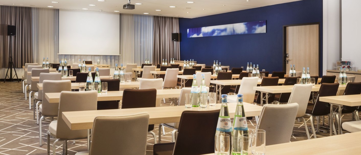 Moderner Konferenzraum mit Reihen von Tischen und St&uuml;hlen, ausgestattet mit Wasserflaschen und Gl&auml;sern. Eine Leinwand und Vorh&auml;nge sind sichtbar., &copy; Park Inn by Radisson Stuttgart, Jonathan Cosh Visual Eye