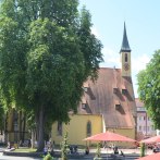 The Kreuzkirche Nürtingen church with its striking tower, surrounded by green trees and red parasols on a sunny square., © kkmaisch_gf