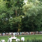 Lange Tafel im Freien, umgeben von Bäumen. Menschen sitzen an festlich gedeckten Tischen im Park von Burg Schaubeck. Sommerliche Atmosphäre., © GFA_GF