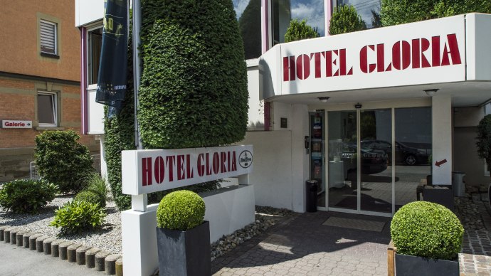 Eingang des Hotel Gloria mit gro&szlig;em Schild und gepflegten Pflanzen. Moderne Glasfront und dekorative Str&auml;ucher umrahmen den Eingang., &copy; Hotel Gloria