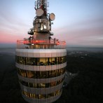 A television tower with an illuminated viewing platform at sunset. The sky is tinged pink and the landscape stretches out in the background., © SWR Media Services GmbH / Achim Mende