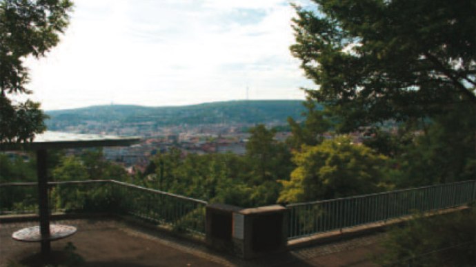 Aussichtsplattform mit Geländer, umgeben von Bäumen, bietet Blick auf eine Stadt und Hügel im Hintergrund., © Stuttgart-Marketing GmbH
