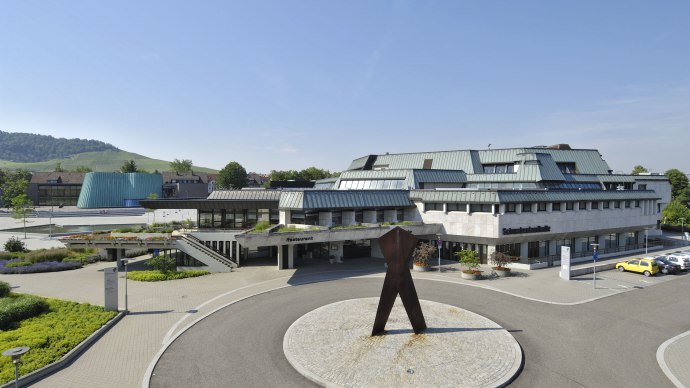 Die Schwabenlandhalle Fellbach mit moderner Architektur, umgeben von Grünflächen und einer Skulptur im Vordergrund. Im Hintergrund sind Hügel zu sehen., © Peter Hartung