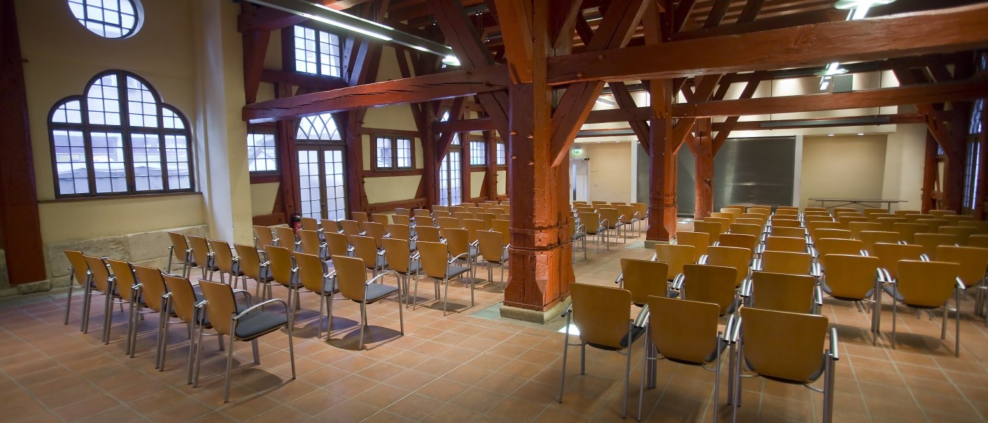 Innenansicht der Schickhardt-Halle im Alten Rathaus mit roten Holzträgern und leeren Stuhlreihen auf einem Fliesenboden., © Esslingen live Innenansicht der Schickhardt-Halle im Alten Rathaus mit roten Holzträgern und leeren Stuhlreihen auf einem Fliesenboden., © Esslingen live