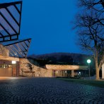 Modern architecture with glass roof at night, next to an illuminated historical building. Cobblestones in the foreground, trees in the background., © Congress-Centrum Stadtgarten Schwäbisch Gmünd