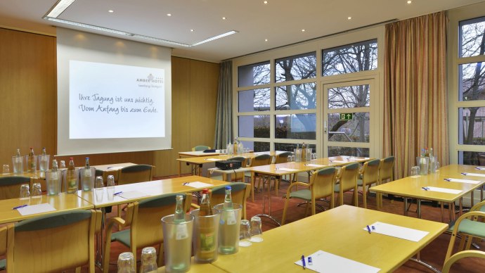 Tagungsraum im Amber Hotel Leonberg/Stuttgart mit Tischen, Stühlen, Wasserflaschen und einer Präsentationsleinwand., © DH STUDIO Dirk Holst