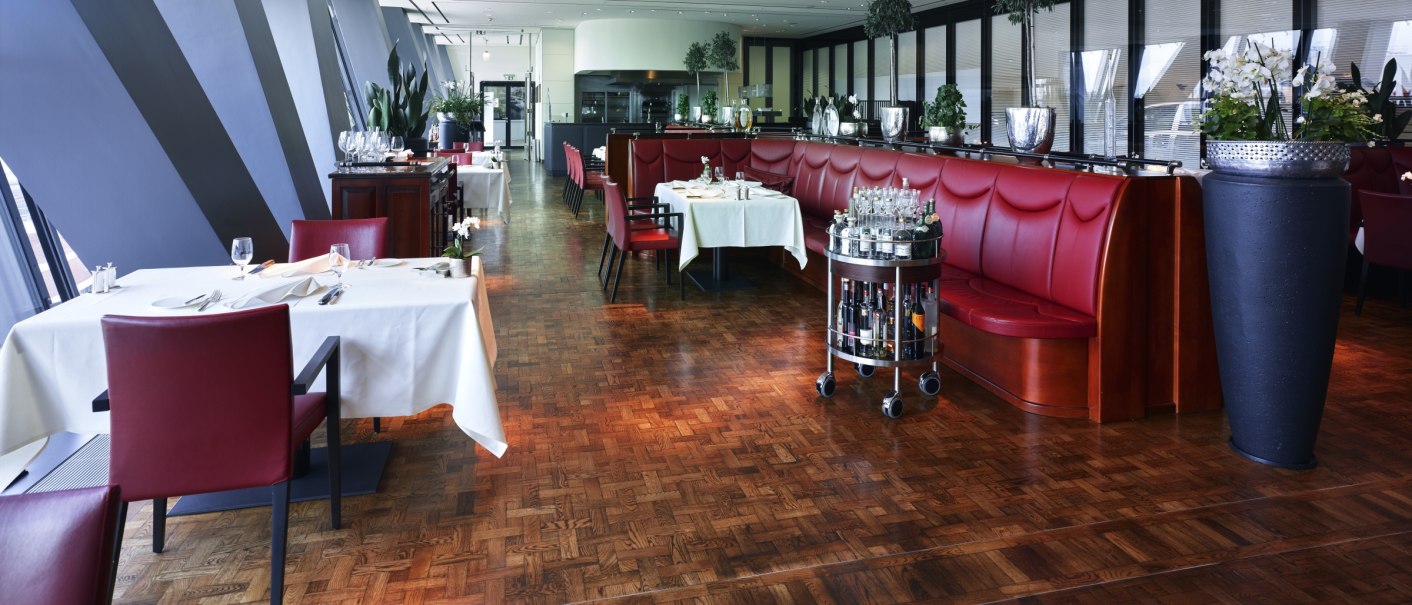 Elegant restaurant with red benches, white-clothed tables and plants. Wooden floor and modern architecture create a stylish atmosphere., © Dr. Ing. h.c. F. Porsche AG