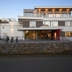 Modern building exterior with glass balconies, lighting and bicycles in the foreground. Evening mood with clear blue sky., © Architekurbuero-Gaysert