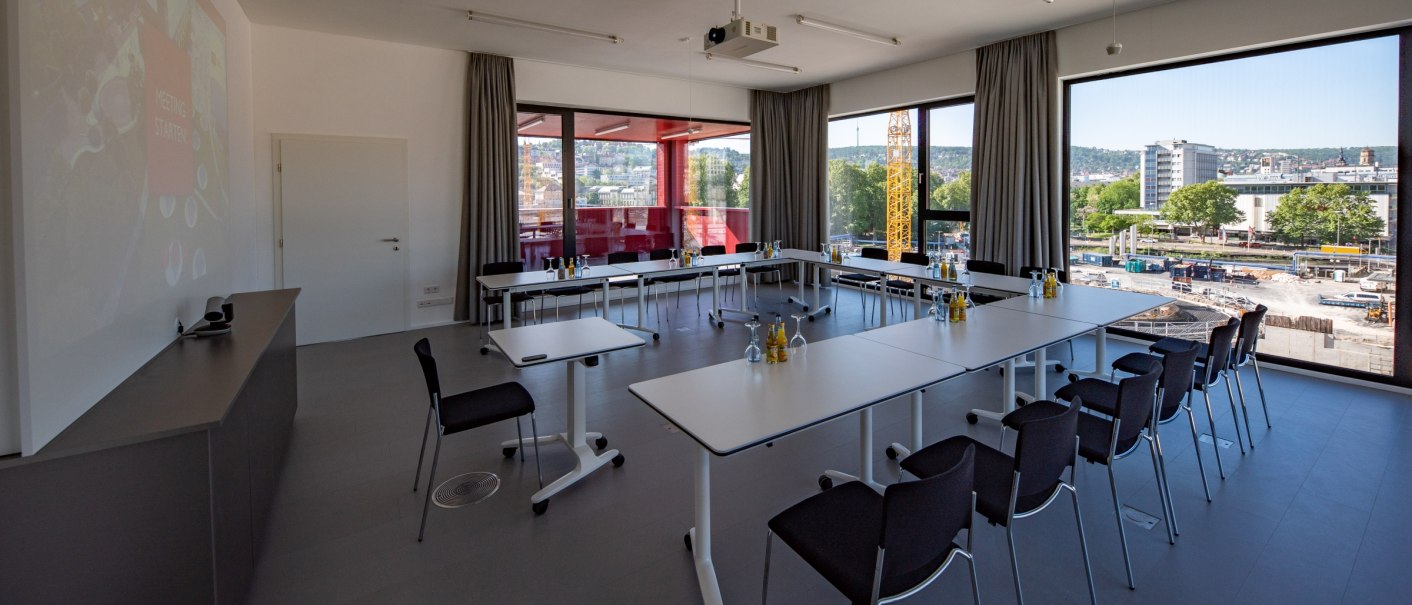 Moderner Konferenzraum mit U-förmiger Tischanordnung, großen Fenstern und Blick auf eine Baustelle in Stuttgart. Helle, minimalistische Einrichtung., © Thomas Niedermüller