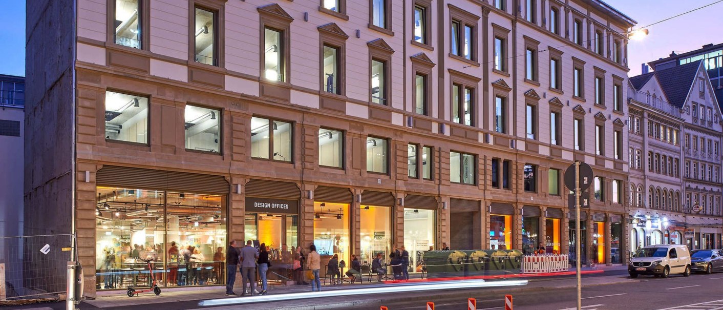Bürogebäude bei Abenddämmerung, beleuchtete Fenster, Menschen vor dem Eingang. Moderne Architektur mit klassischer Fassade., © Design Offices Bürogebäude bei Abenddämmerung, beleuchtete Fenster, Menschen vor dem Eingang. Moderne Architektur mit klassischer Fassade., © Design Offices