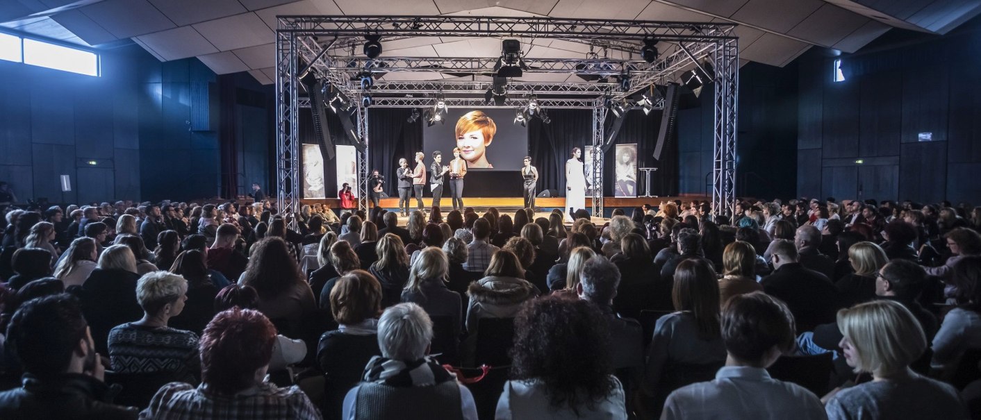Großer Saal mit Publikum, das auf eine Bühne mit Präsentation blickt. Eine große Leinwand zeigt ein Bild, während mehrere Personen auf der Bühne stehen., © eslive Großer Saal mit Publikum, das auf eine Bühne mit Präsentation blickt. Eine große Leinwand zeigt ein Bild, während mehrere Personen auf der Bühne stehen., © eslive