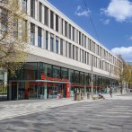 The SparkassenForum Böblingen with its modern glass façade and pedestrian zone. People strolling in sunny weather. Trees with fresh leaves., © ccbs