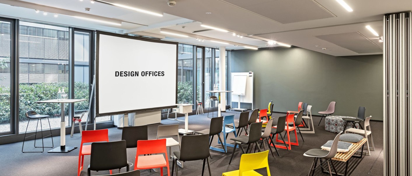 Modern training room with colorful chairs, screen and flipchart. Large windows let in plenty of light. The room feels open and inviting., © Design Offices