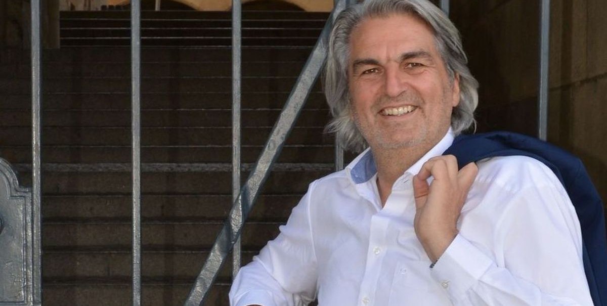 Ein Mann in weißem Hemd lehnt lächelnd an einem Gittertor. Im Hintergrund sind Treppen und ein historisches Gebäude zu sehen., © Wolfgang Seljé