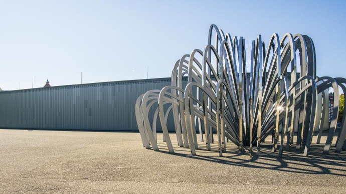 Moderne Skulptur aus gebogenen Metallstreben vor der Galerie Stihl in Waiblingen, bei klarem Himmel und Sonnenschein., © SMG, Sarah Schmid Moderne Skulptur aus gebogenen Metallstreben vor der Galerie Stihl in Waiblingen, bei klarem Himmel und Sonnenschein., © SMG, Sarah Schmid