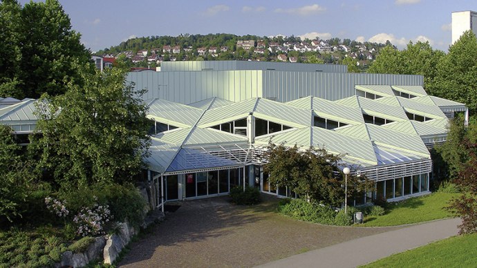 Die Stadthalle Leonberg mit ihrem markanten, geometrischen Dachdesign, umgeben von B&auml;umen und Gr&uuml;nfl&auml;chen, bei sonnigem Wetter., &copy; Stadthalle Leoonberg