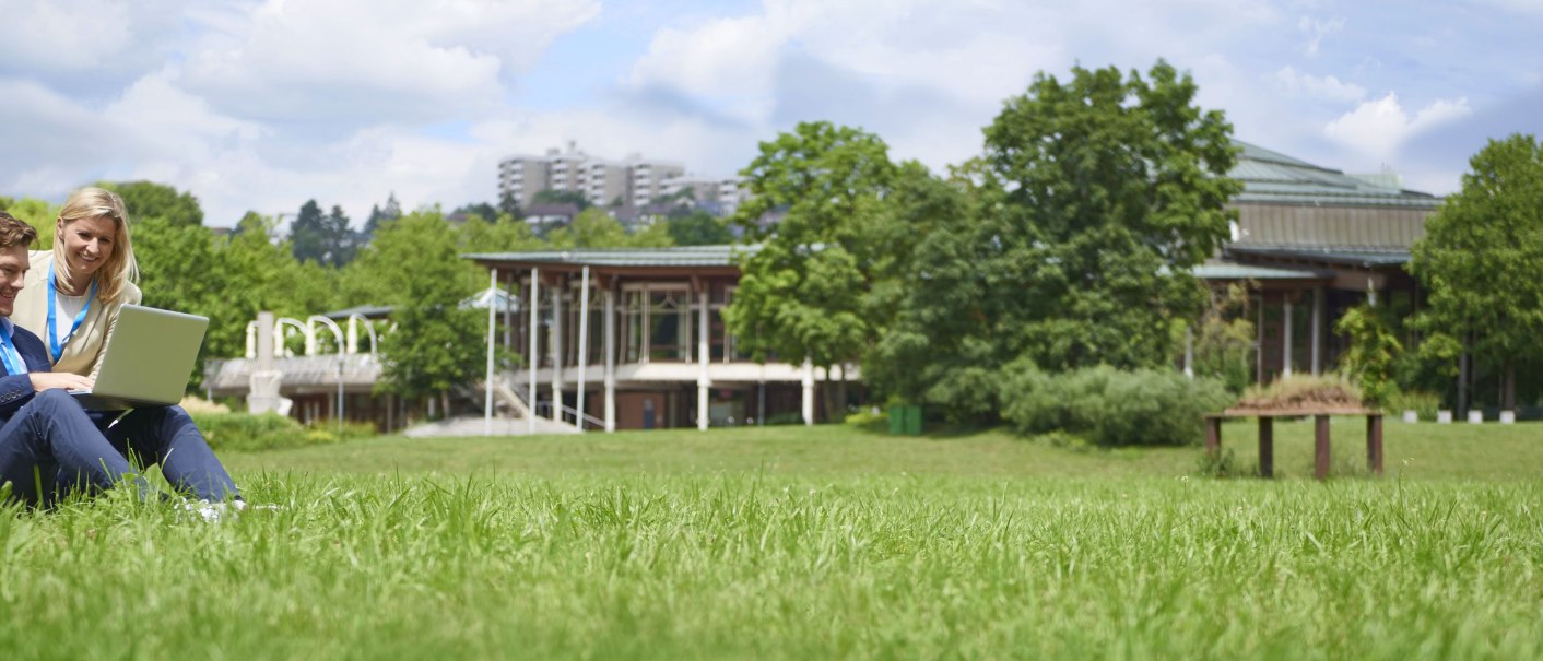 Zwei Personen sitzen auf einer Wiese mit einem Laptop. Im Hintergrund ist das Bürgerzentrum Waiblingen zu sehen, umgeben von Bäumen und Grünflächen., © Peter Oppenländer Zwei Personen sitzen auf einer Wiese mit einem Laptop. Im Hintergrund ist das Bürgerzentrum Waiblingen zu sehen, umgeben von Bäumen und Grünflächen., © Peter Oppenländer