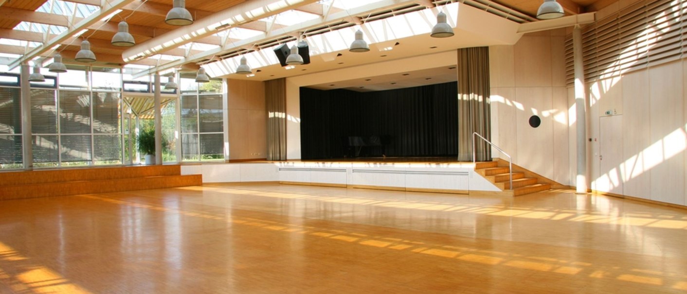 Großer, heller Saal mit Holzboden, Bühne und vielen Fenstern. Die Decke ist mit großen Lampen ausgestattet., © Gemeinde Aichwald Großer, heller Saal mit Holzboden, Bühne und vielen Fenstern. Die Decke ist mit großen Lampen ausgestattet., © Gemeinde Aichwald