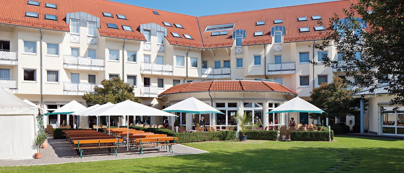 Das Seminaris Hotel Bad Boll zeigt eine Terrasse mit Sonnenschirmen und Sitzgelegenheiten vor einem großen Gebäude mit rotem Dach., © Seminaris Hotels