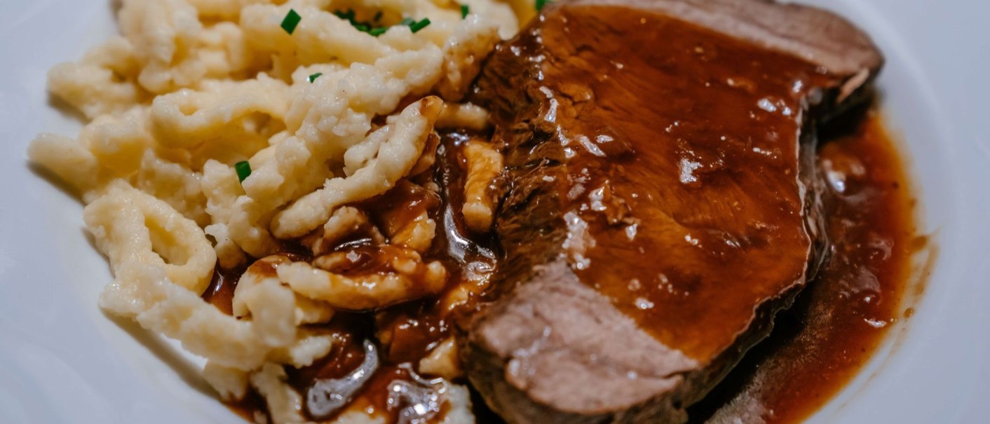 Ein Teller mit Spätzle und einem Stück Braten, übergossen mit dunkler Soße. Die Spätzle sind mit Schnittlauch garniert., © Thomas Niedermüller