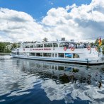 Das Passagierschiff MS Wilhelma fährt auf einem Fluss. Der Himmel ist blau mit Wolken. Menschen stehen an Bord, und eine deutsche Flagge weht am Heck., © all copyrights are reserved by maks richter
