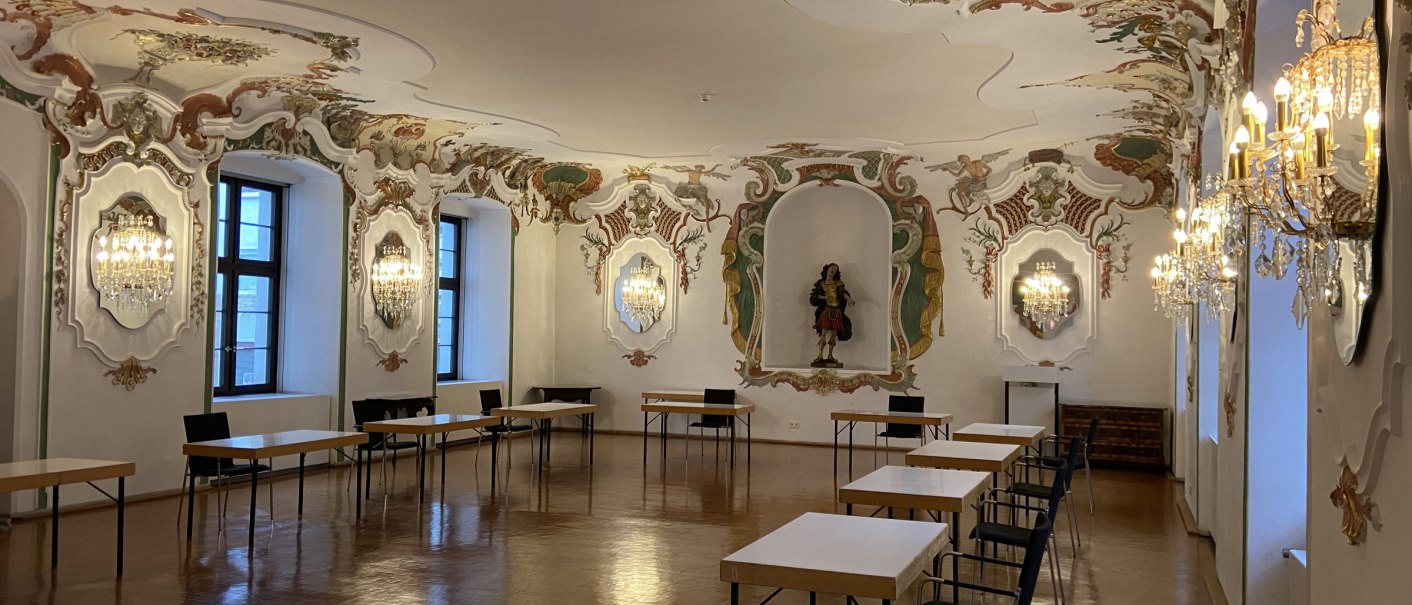 Baroque room with ornate stucco decorations and chandeliers. Tables and chairs are arranged along the walls., © Kulturzentrum Prediger