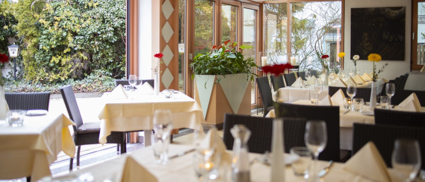 Elegantes Restaurant im Wintergartenstil mit gedeckten Tischen, wei&szlig;en Tischdecken und Blumen. Gro&szlig;e Fenster bieten Blick auf den Garten., &copy; Hotel Gloria