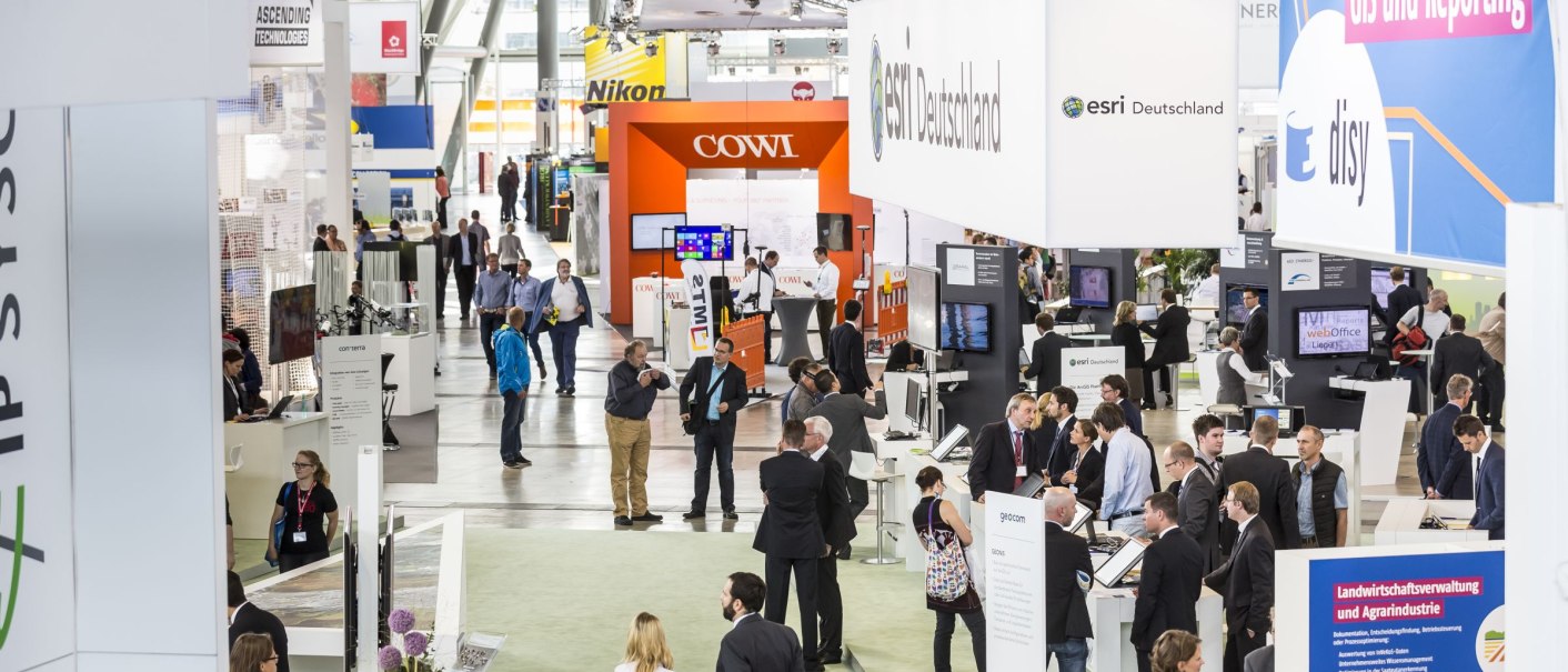 Visitors at the Stuttgart trade fair in a hall with various stands and company logos such as esri Germany and disy., &copy; Messe Stuttgart
