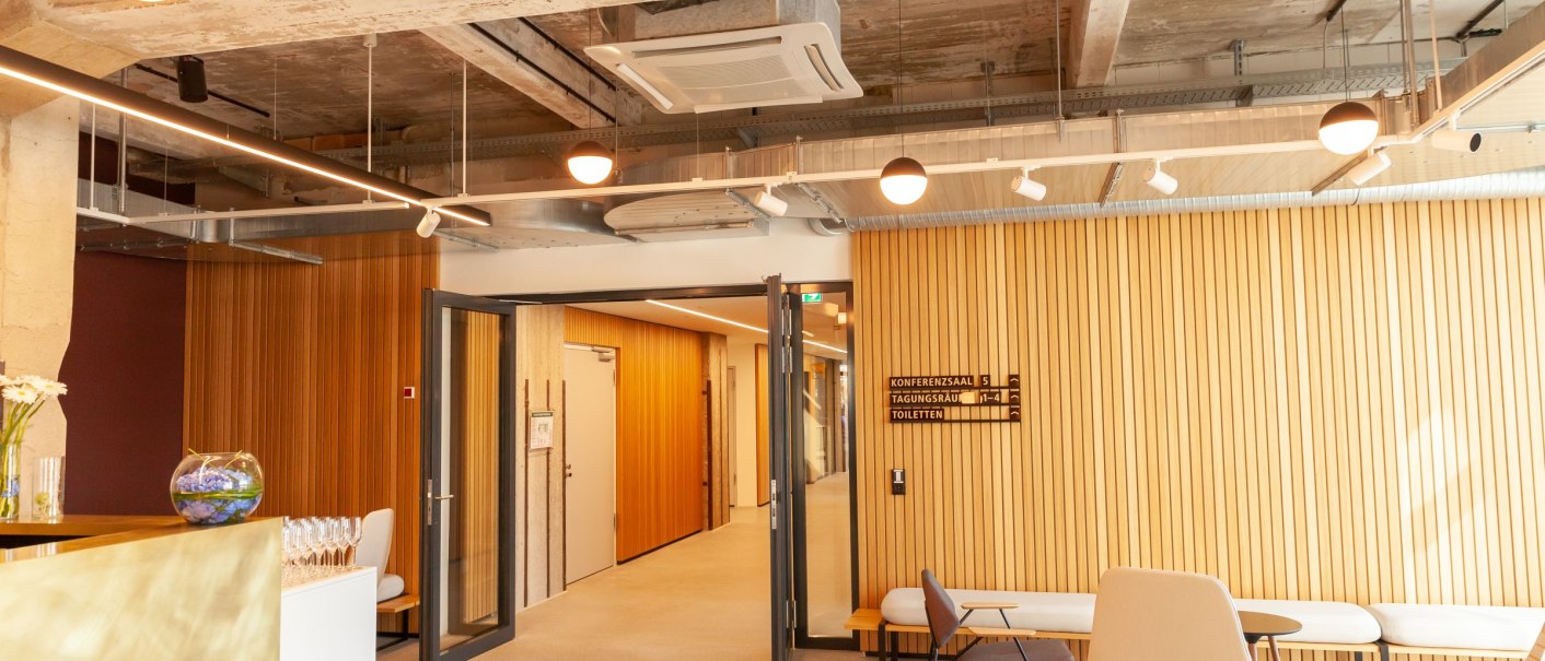 Modern foyer with wooden walls, seating and round ceiling lights. A sign indicates conference rooms and restrooms., © Stefan Baraniecki