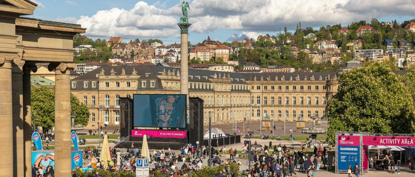 People gather in front of a large screen on Schlossplatz in Stuttgart. The New Palace can be seen in the background., &copy; SMG, Sarah Schmid
