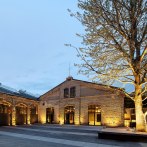 Illuminated carriage sheds with brick façade at dusk, tree in the foreground. Historic architecture with modern elements., © Wagenhallen Stuttgart GmbH & Co. KG