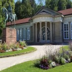 Der Kursaal Bad Cannstatt mit klassischer Fassade, Reiterstatue und bunten Blumenbeeten im Vordergrund an einem sonnigen Tag., © smg