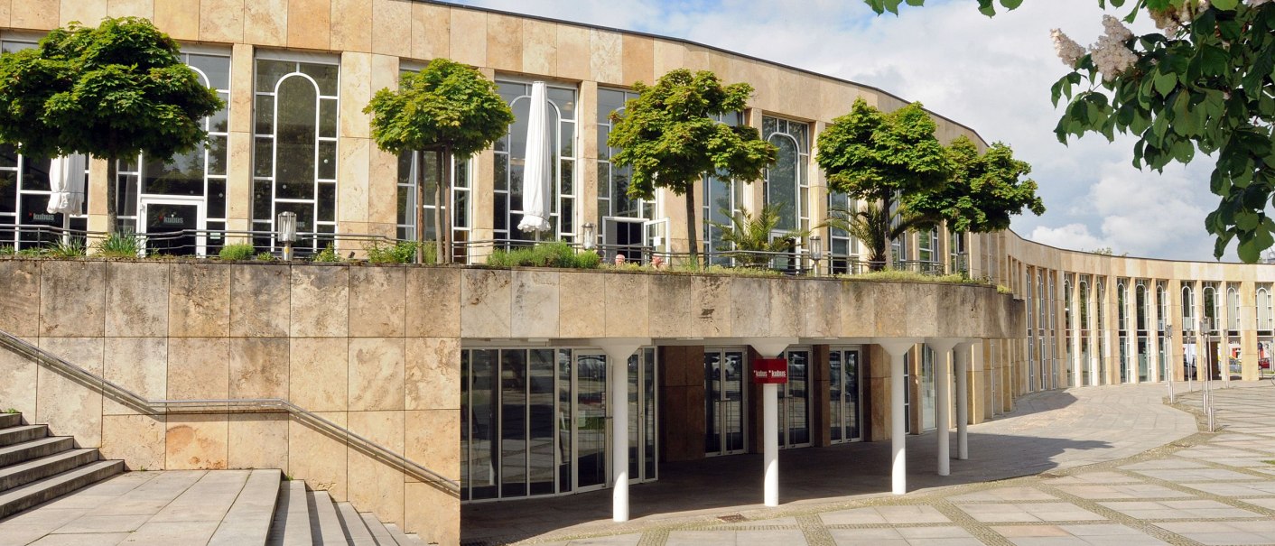 Das Forum am Schlosspark zeigt eine moderne Fassade mit großen Glasfenstern und Bäumen auf einer Terrasse. Der Himmel ist blau mit einigen Wolken., © Wolfgang List
