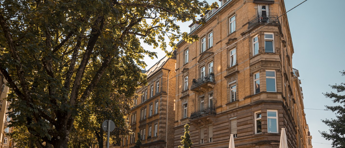Historisches Gebäude an einer Straßenecke, umgeben von Bäumen und geparkten Autos. Sonniger Tag mit klarem Himmel., © SMG Stuttgart Marketing GmbH - Sarah Schmid