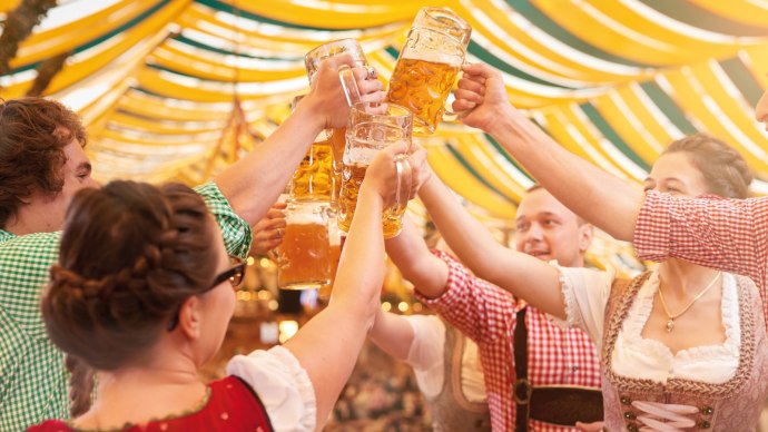 Gruppe in Tracht st&ouml;&szlig;t mit Bierkr&uuml;gen in einem festlich dekorierten Bierzelt an. Fr&ouml;hliche Stimmung unter gelb-gr&uuml;nen Stoffbahnen., &copy; Stuttgart-Marketing GmbH, Jean-Claude Winkler