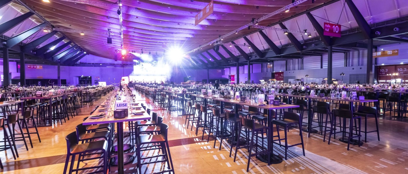 Innenansicht der Paul Horn Halle 10 in der Messe Stuttgart, mit langen Tischreihen und lila Beleuchtung., © Messe Stuttgart