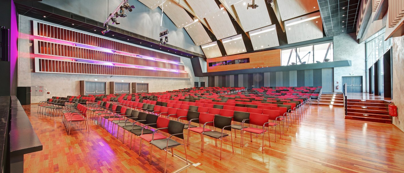 Großer Saal mit roten und schwarzen Stühlen, Holzboden und moderner Beleuchtung. Die Decke ist hoch und architektonisch gestaltet., © eslive_Martin Frey
