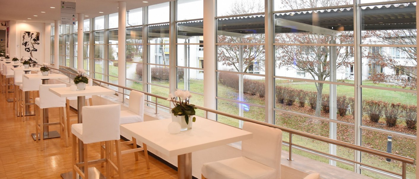 Modernes Foyer mit gro&szlig;en Fenstern, wei&szlig;en Tischen und St&uuml;hlen. Blick auf eine gr&uuml;ne Au&szlig;enanlage mit B&auml;umen., &copy; Filharmonie_gf