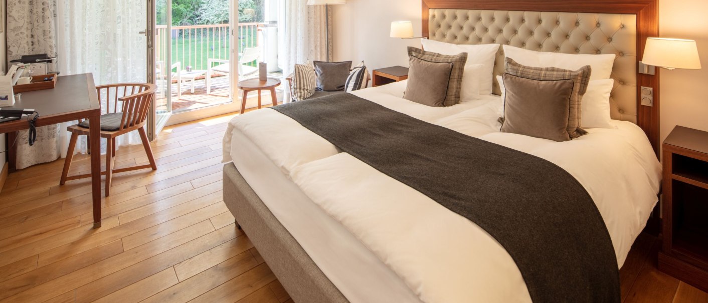 Elegantes Hotelzimmer mit großem Bett, Holzboden, Schreibtisch und Balkon mit Blick ins Grüne., © WHS