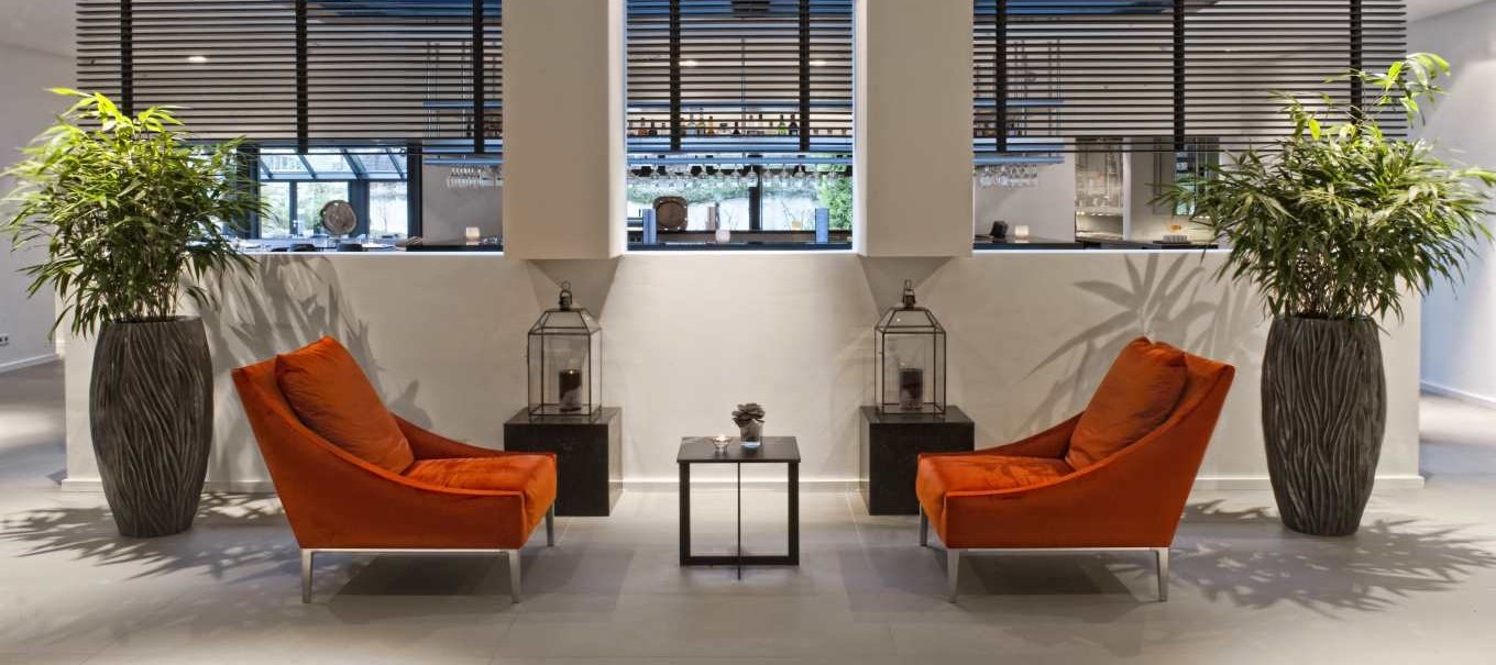 Modern lobby with two orange armchairs, large plant vases and decorative lanterns. Bright, inviting atmosphere., &copy; Wyndham Stuttgart Airport Messe