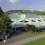 The Stadthalle Leonberg with its striking, geometric roof design, surrounded by trees and green spaces, in sunny weather., © Stadthalle Leoonberg